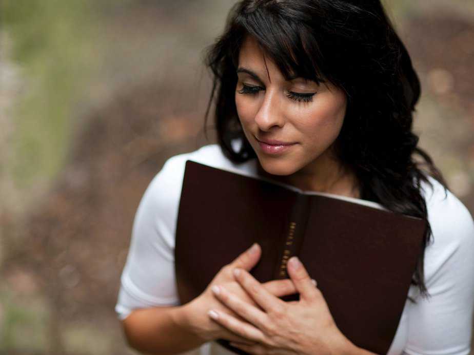 Woman holding open bible close to herself with eyes closed as if praying