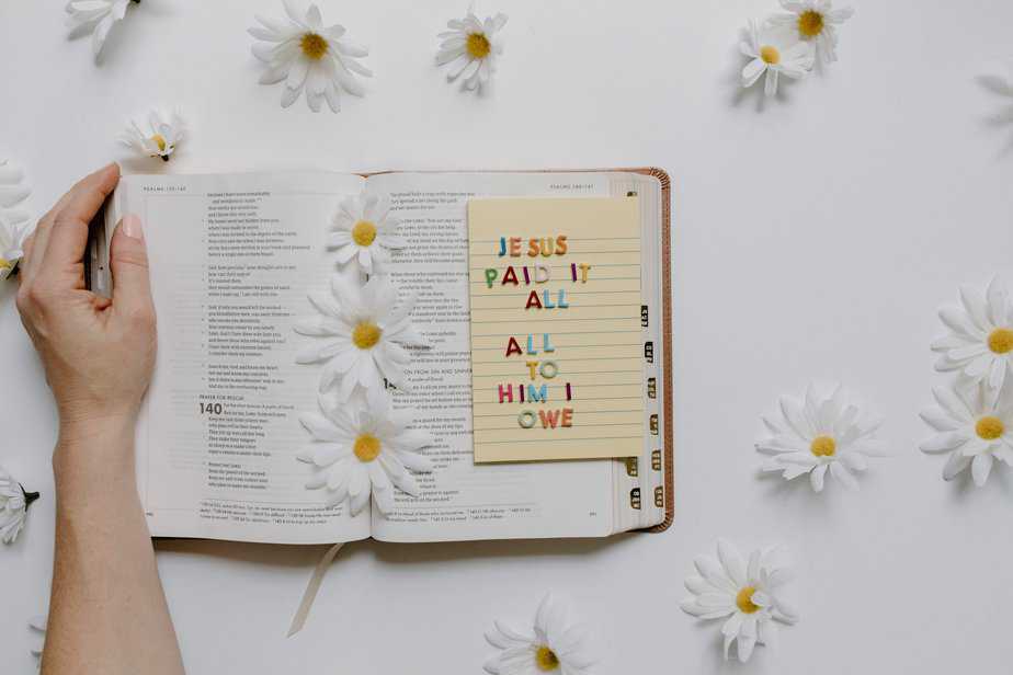 Open Bible on a white table with white sunflowers and a note on the bible with text 