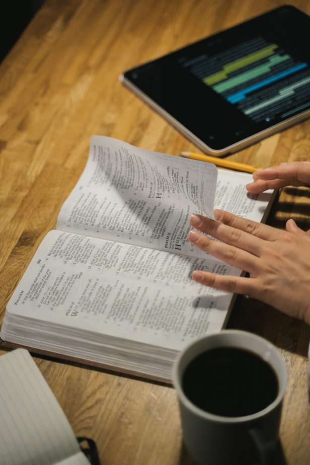 Open Bible on the desk with hands flicking the pages, with a tab and a cup of black coffee at the side